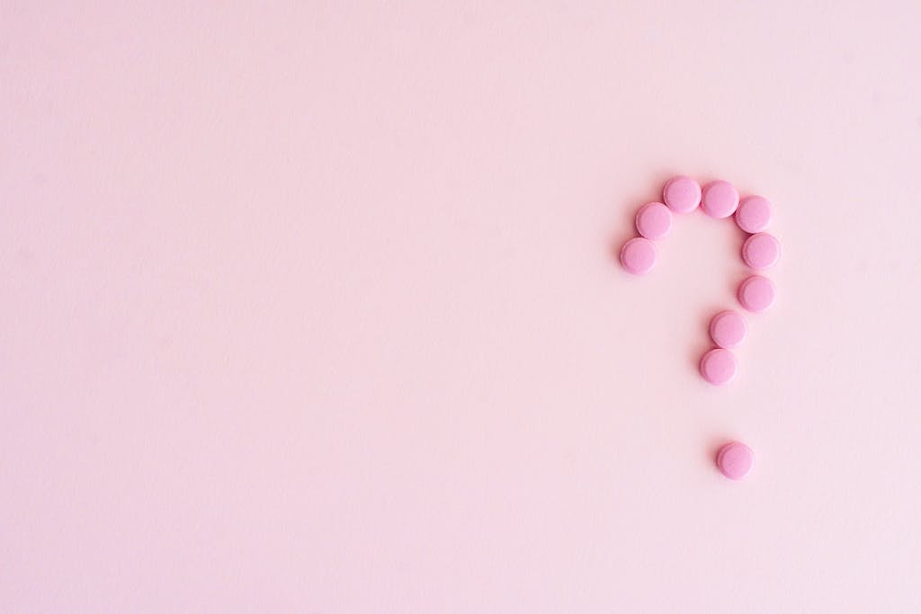 A question mark created from pink pills on a light pink surface, symbolizing uncertainty in health decisions.